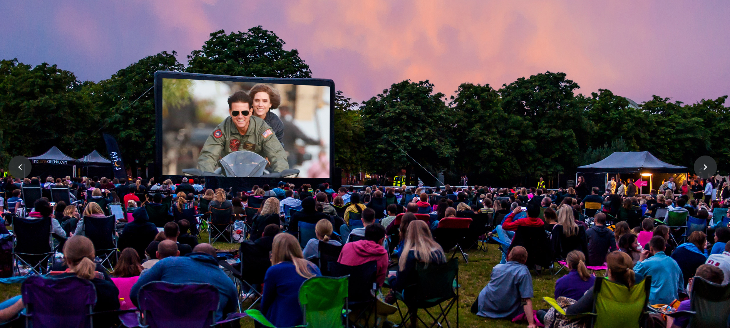 Open air cinema in London: people at a Luna Cinema screening on Clapham Common at dusk, sitting on camping chairs and picnic blankets watching Top Gun on the big screen