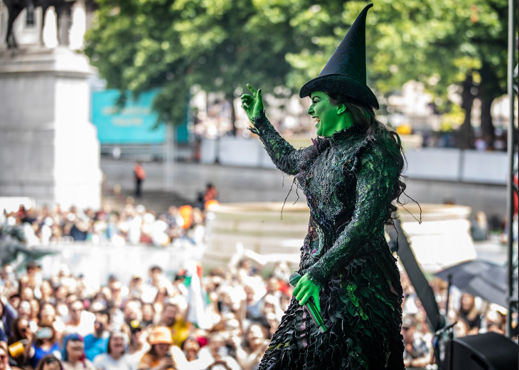 A cast member from Wicked on stage in witch costume and green face paint at a previous West End Live.